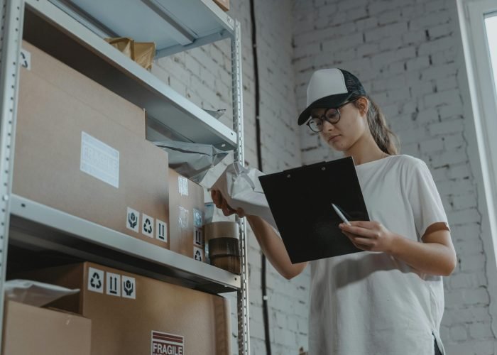 Warehouse worker organizing packages on shelf with clipboard.